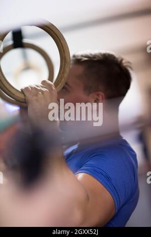Fitness uomo bello fare immersione esercizio utilizzando anelli in palestra Foto Stock