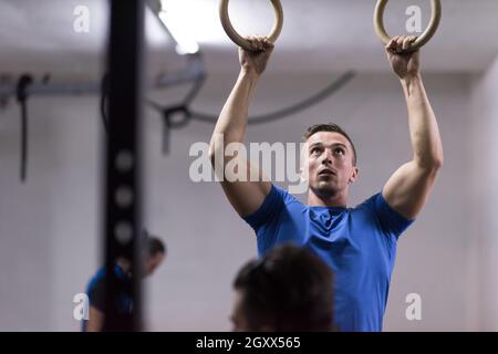 Fitness uomo bello fare immersione esercizio utilizzando anelli in palestra Foto Stock