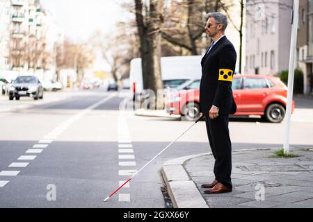 Cieco camminando sul marciapiede stecco di presa che indossa fascia da braccio Foto Stock