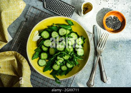 Ciotola di cetriolo e insalata di rucola con olio d'oliva e semi di sesamo nero Foto Stock