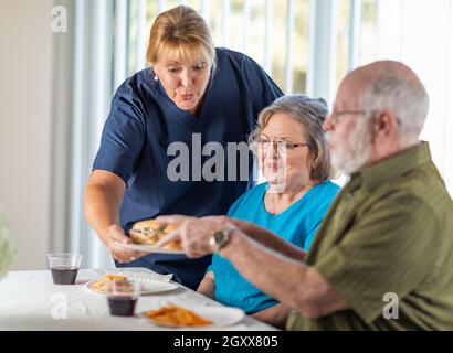 Donne medico o infermiere che serve Senior Adulto Giovane sandwiches nella tabella. Foto Stock