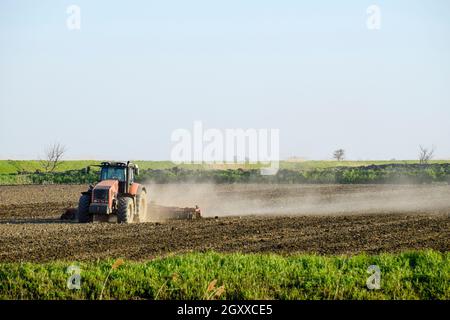 Un trattore con un aratro stabilisce il terreno. La coltivazione del suolo sul campo per la semina. Foto Stock