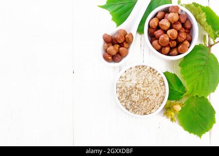 Farina e nocciole in due ciotole, un cucchiaio con noccioli di noce pelati e un ramo di filbert con foglie sullo sfondo di tavola di legno dall'alto Foto Stock