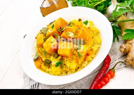 Porridge di miglio con salsa piccante di zucca e semi in un piatto su un asciugamano, pepe caldo, radice di zenzero, aglio e prezzemolo su sfondo di tavola di legno Foto Stock