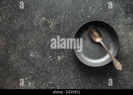 Piatto vintage vuoto con cucchiaio argento su tavolo nero. Vista dall'alto. Foto Stock