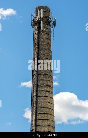 Camino alto presso l'impianto con attrezzature per la radiodiffusione. Installazione di un'antenna cellulare. Combinazione di camini di fabbrica e alta tecnologia Foto Stock