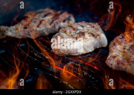 Bistecche di maiale alla griglia con fiamme. Foto Stock