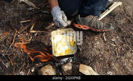 persona che cucinano le uova fritte nella natura campeggio all'aperto, fornello preparare la prima colazione pic-nic strapazzate su una padella di metallo. Foto Stock