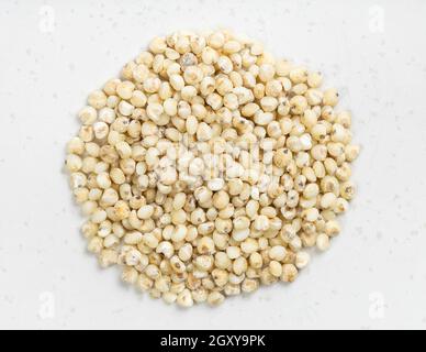 Vista dall'alto del cumulo di groat di Sorghum grezzi e lucidati vicino su una piastra in ceramica grigia Foto Stock