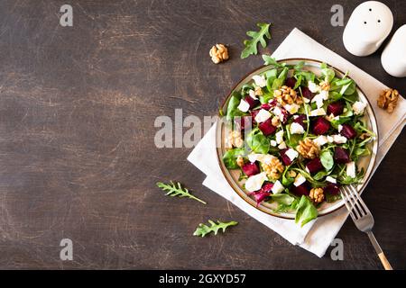 Insalata di barbabietole o barbabietole con rucola fresca, formaggio morbido e noci sul piatto, condimento e spezie su sfondo di legno scuro, spazio copia, vista dall'alto/ Foto Stock