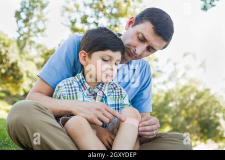 Padre amorevole mette una benda sul gomito del suo giovane figlio nel parco. Foto Stock