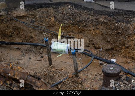 Scavato il marciapiede rivelando i fili in tubi di protezione. Costruzione di linee elettriche o cavi per telecomunicazioni, costruzione di rete ottica informaz Foto Stock