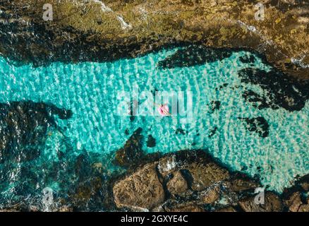 Femmina che galleggia in un giocattolo ad anello a forma di ciambella nel oceano con idilliaca acqua blu cristallo Foto Stock