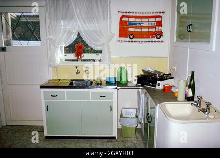 Una cucina molto essenziale in un appartamento o appartamento in un sobborgo di Sydney, NSW, Australia nel 1973. E' interessante notare che anche se non è ben attrezzata (con solo un piccolo plug-in, piano di lavoro e grill), contiene due lavandini! Per la decorazione c'è un té-tovagliolo di un autobus londinese fissato al muro questa immagine è da una vecchia trasparenza di colore Kodak dilettante – una fotografia d'epoca anni '70. Foto Stock