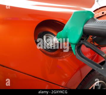 Ugello verde per la pompa del gas benzenico che riempie il serbatoio arancione per auto sportive. Primo piano Foto Stock