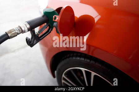 Ugello verde per la pompa del gas benzenico che riempie il serbatoio arancione per auto sportive. Primo piano Foto Stock