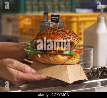 Uno chef prepara un hamburger per un cliente. La donna prende la scatola dell'hamburger e la consegna al cliente. Ambiente di lavoro in cucina nel backgro Foto Stock