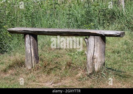 Rustico posto a panca in legno del parco fatto di due tronchi di tronco di albero tagliato con una tavola attraverso la parte superiore e uno sfondo di erba. Foto Stock