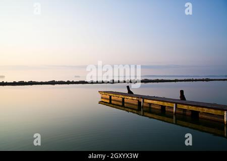 Lungo molo di legno si estende in un lago tranquillo in una giornata limpida Foto Stock