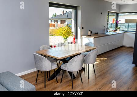 Una moderna sala da pranzo collegata al soggiorno e alla cucina, ci sono grandi finestre nella parete, un tavolo a vista e sedie. Foto Stock