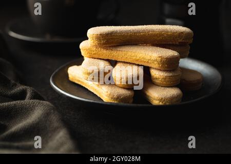 Biscotto italiano savoiardi. Biscotti dolci. Biscotti di spugna tiramisù su tavola nera. Foto Stock