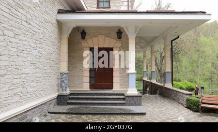 Porta d'ingresso in legno a una grande casa privata moderna ed elegante con piastrelle sul marciapiede e giardino posteriore Foto Stock
