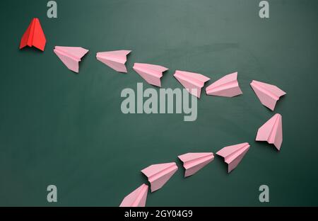 Gruppo di aeroplani di carta rosa che seguono il primo rosso su sfondo verde. Il concetto di unire un team per raggiungere gli obiettivi, un leader forte, un alto Foto Stock