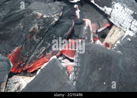 Fuoco su tronchi in pentola di fuoco con braci e carbone che brucia. Falò con fiamme rosse e arancioni. Fuoco sfondo con boschi e tavole sul fuoco Foto Stock