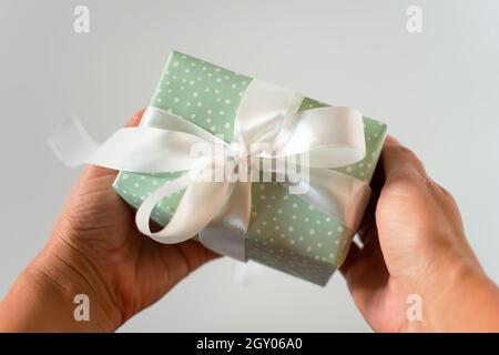 Primo piano con le mani del regalo. Un piccolo regalo di un delicato pacchetto di menta con un nastro di raso bianco neve nelle mani della madre femminile. Il concetto di vacanza, va Foto Stock