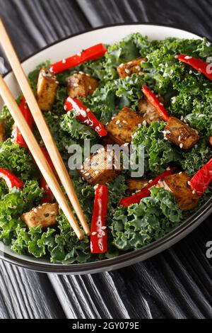 Insalata di tofu Teriyaki con peperoni, kale e semi di sesamo da vicino in una ciotola sul tavolo. Verticale Foto Stock