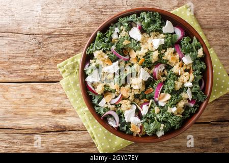 Insalata senza glutine preparata con quinoa, cipolle, verdure del collardo, feta e mandorle condite con olio vegetale in una ciotola sul tavolo. Orizzontale a. Foto Stock