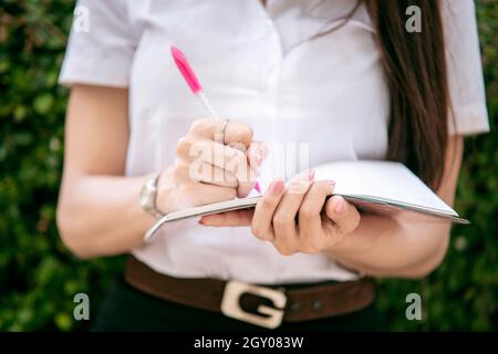 Donna che scrive i suoi pensieri nel taccuino. Ragazza sta scrivendo le note e progettando il suo programma sul diario del taccuino nel fuoco selettivo. Primo piano Foto Stock