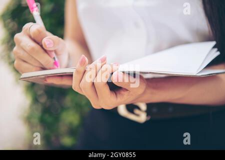 Donna che scrive i suoi pensieri nel taccuino. Ragazza sta scrivendo le note e progettando il suo programma sul diario del taccuino nel fuoco selettivo. Primo piano Foto Stock