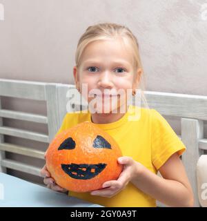 La ragazza mostra una zucca con una faccia paurosa dipinta, creando una Lanterna Jack Halloween. Halloween partito e famiglia sfondo stile di vita Foto Stock