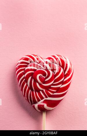 Delizioso lecca lecca lecca a forma di cuore cucita su un bastone di legno con il tipo rosa sullo sfondo. Foto Stock