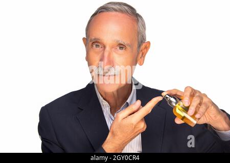 Uomo d'affari maturo sorridente in tuta mostrando anti-invecchiamento lozione prodotto, godendo la sua pelle perfetta del viso, guancia, pimple, whelk, pustule, secco, oliato, pro Foto Stock