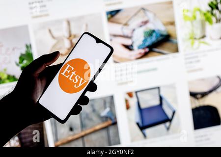 Uno smartphone con il logo Etsy in una mano sullo sfondo del catalogo di siti Web. Foto Stock