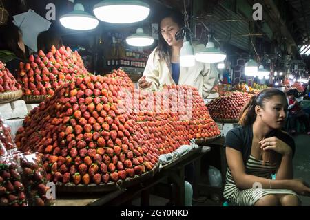 Due donne accanto a mucchi di fragole fresche in un mercato coperto nella città di Baguio, Filippine Foto Stock