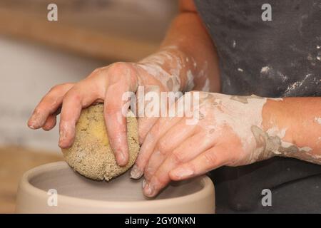 Lavorare con l'argilla in uno studio di ceramica gettando una pentola sulla ruota del vasaio Foto Stock