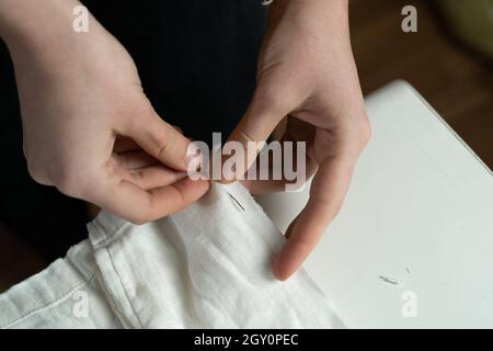 Il primo piano di un dressmaker ha cucito il tessuto di cotone bianco per un vestito con un ago e un filo. Studio di cucito. Foto Stock