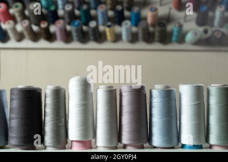 Diverse leggere bobine di filo per cucire e ricamare su un tavolo di legno bianco. Laboratorio di cucito. Foto Stock