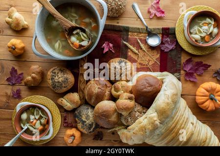 Vista dall'alto verso il basso delle ciotole della zuppa di tacchino e di una cornucopia di pane con panini e panini che si versano fuori. Foto Stock