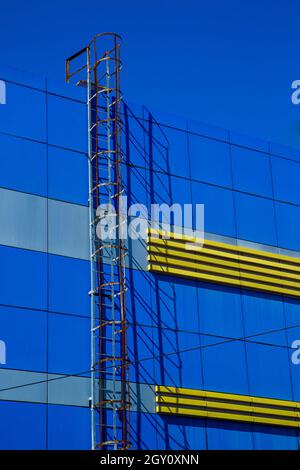 Scala antincendio sulla parte superiore dell'edificio. Scala su una casa blu con inserti gialli, contro un cielo blu. Foto Stock