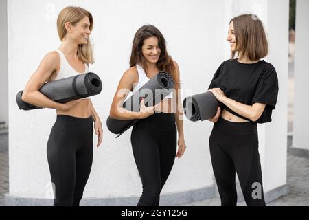 Le ragazze si alzano con i tappetini per il fitness e parlano all'aperto Foto Stock