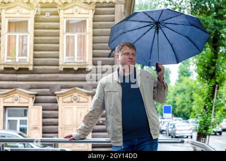 Un uomo di 40-45 anni in giacca bianca con un ombrello in mano gode del tempo autunnale. Foto Stock