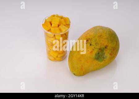 Cubi di mango maturi o pezzi tagliati disposti in vetro trasparente con mango posto vicino su sfondo bianco. Foto Stock