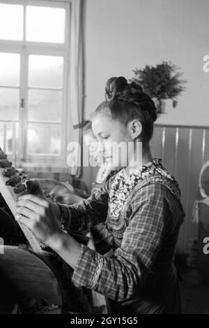 Eine Zigarrenrollerin in Marburger Tracht bei der Arbeit in einer Zigarrenfabrik bei Marburg, Deutschland 1930er Jahre. Una femmina di sigaro a rulli che indossa un abito di Marburg / costume di lavorare in un tessuto di sigaro vicino a Marburg, Germania 1930s. Foto Stock