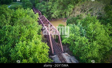 Vista aerea sopra il grande ponte di metallo per i binari ferroviari sul fiume circondato da alberi verdi Foto Stock