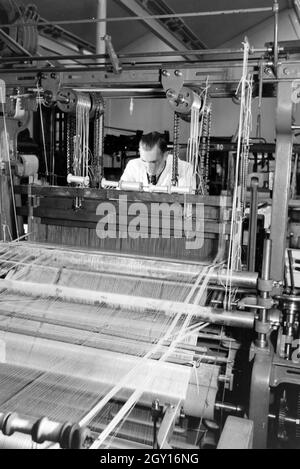 Ein Angestellter einer Textilfirma in Krefeld justiert das Garn in der großen Webmaschine, Deutschland 1930er Jahre. Un dipendente in una azienda tessile in Krefeld regolando il filo in una grande potenza telaio, Germania 1930s. Foto Stock
