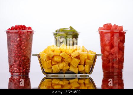 Cocomero, ananas, melograno e fette di kiwi disposte in bicchieri trasparenti con fondo bianco, isolati Foto Stock